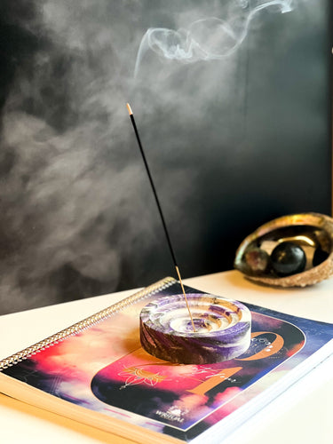 black incense stick, in holder, with a black background and smoke coming from the lit end.